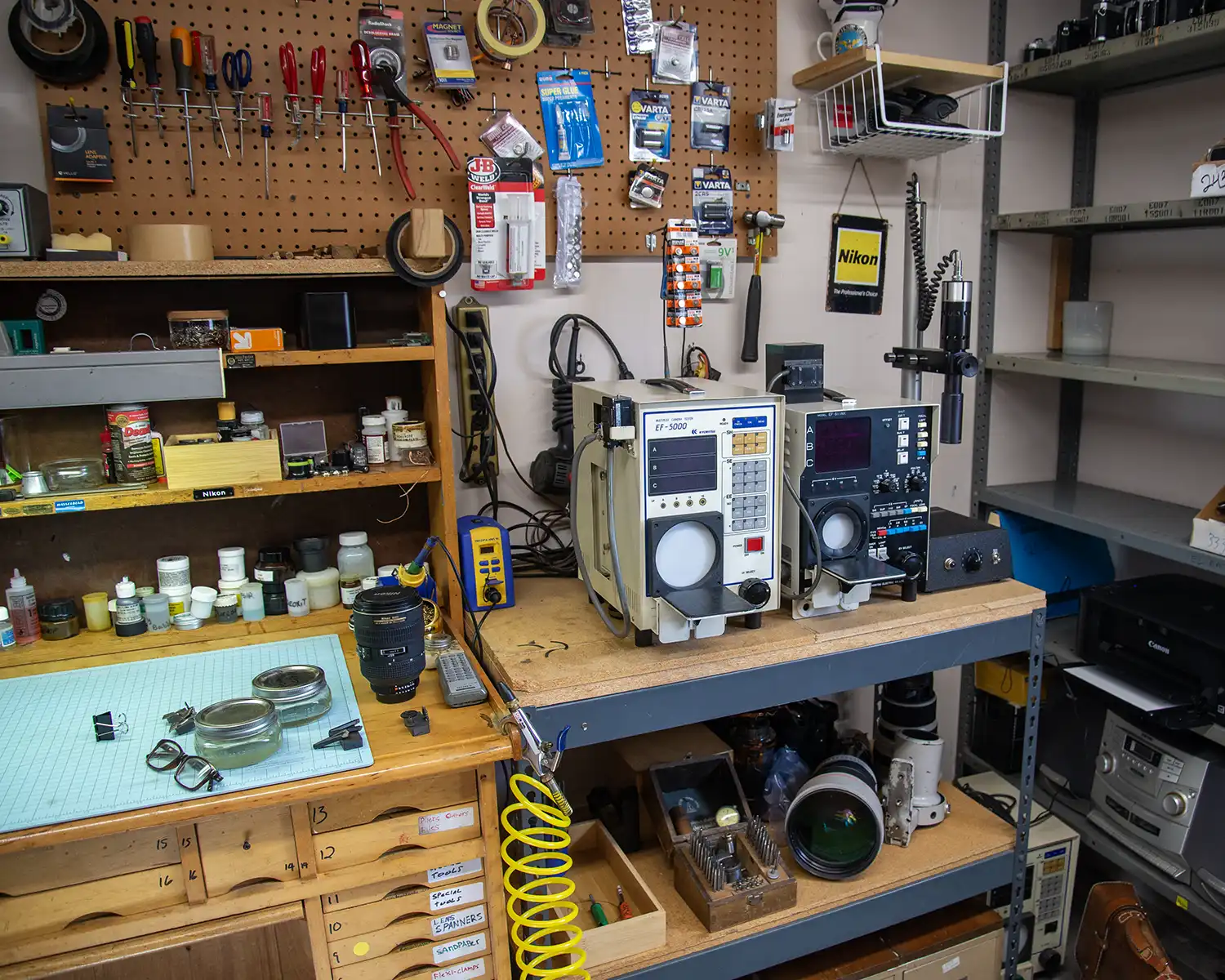Jim's workbench with in-progress lenses out, testing equipment to the right, and tools on shelves and pegboard above the bench.